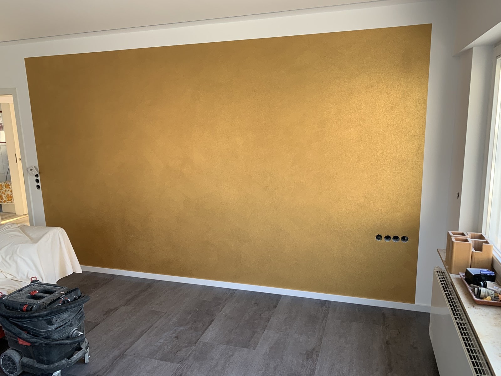 Goldene Metallicbeschichtung als Akzentwand in einem Wohnraum